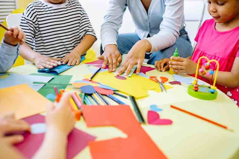 Children's hands cutting and arranging colored paper shapes across a craft table.