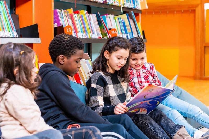 Four children sit together and share a picture book in a colorful school library.